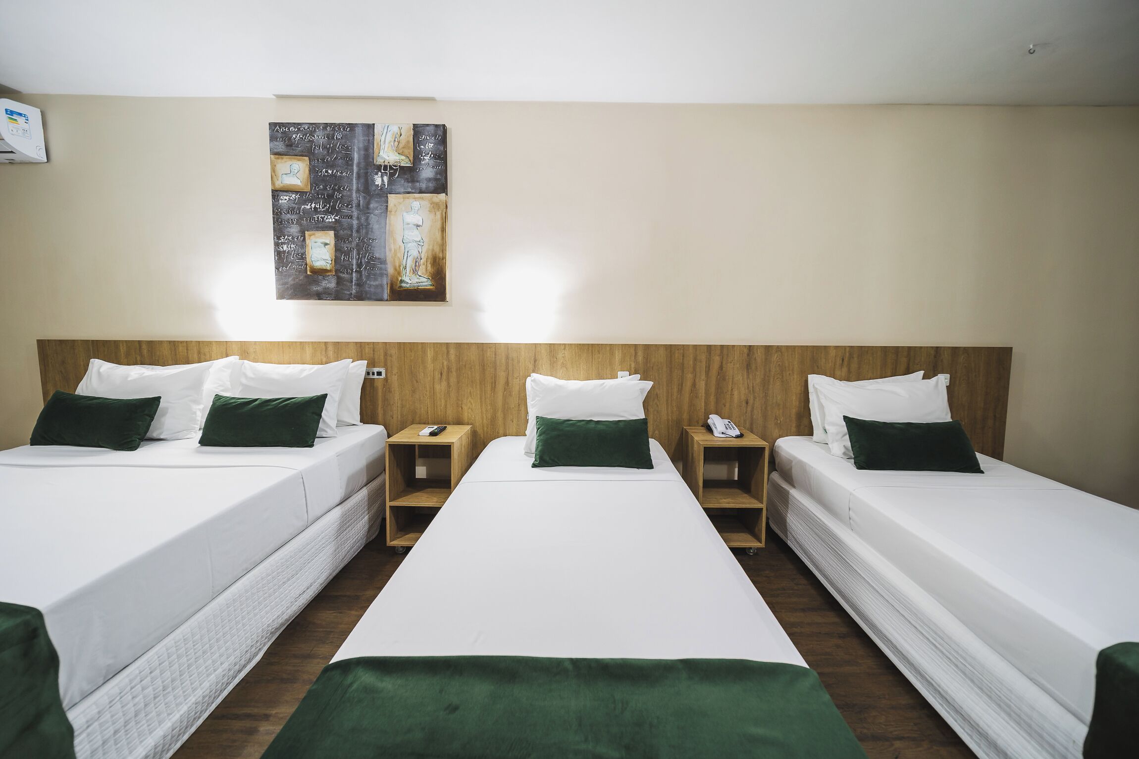 Habitación de hotel con dos camas individuales, cada una con ropa blanca y almohadas verdes, y un cuadro grande en la pared.