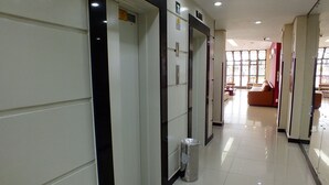 A clean, modern hallway with a trash bin, a fire alarm, and a seating area in the background. - Hotel Nacional Inn Curitiba Torres (Curitiba)