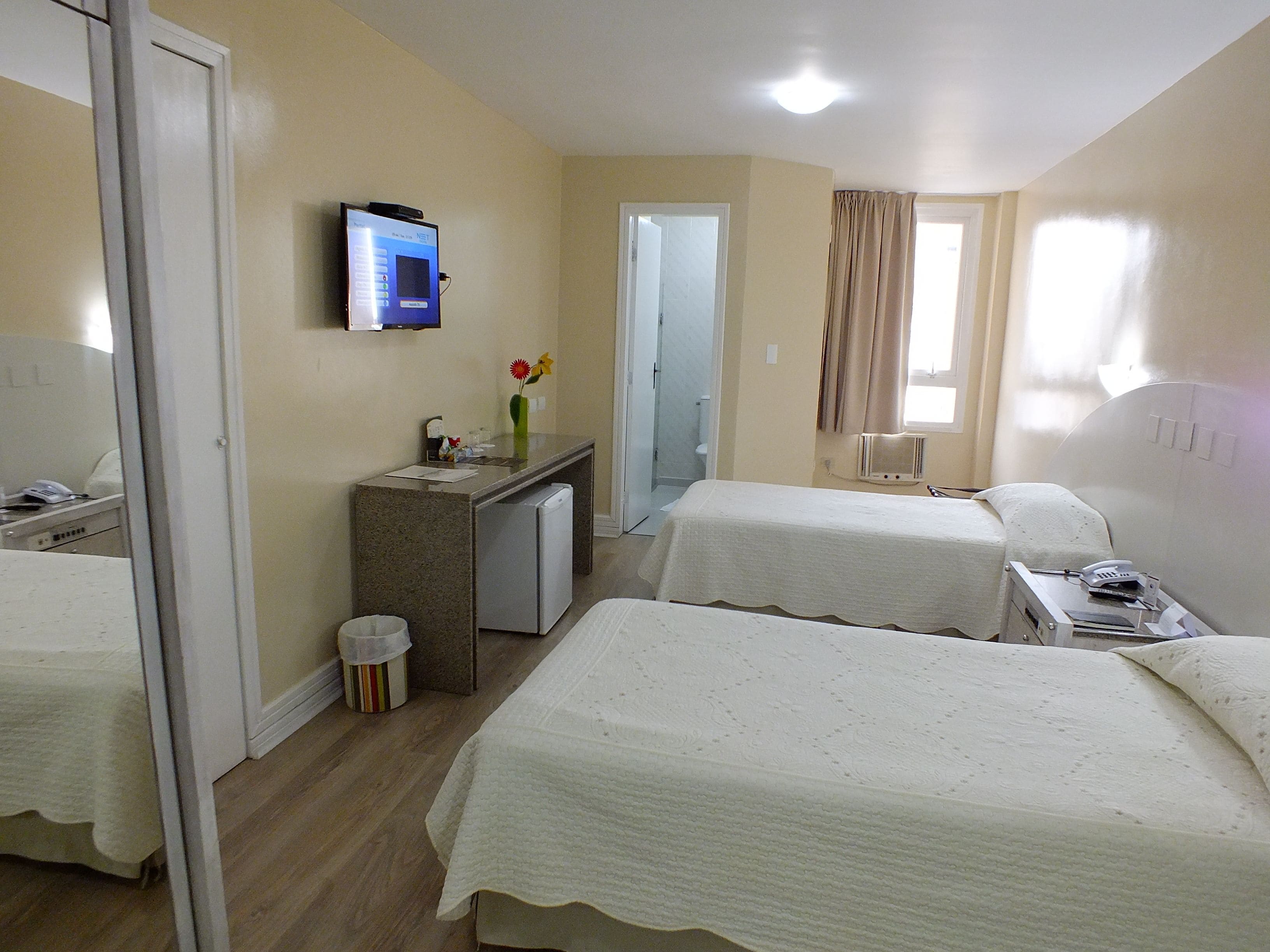 A hotel room with two beds, a small kitchenette, a TV, and a bathroom.