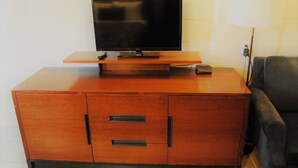 Un meuble de rangement en bois pour appareils électroniques, avec un téléviseur à écran plat, une télécommande et un petit appareil électronique posé sur le dessus.