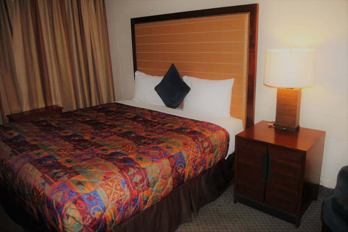 Quarto de hotel com uma cama grande, mesa de cabeceira com abajur e janela com cortinas.