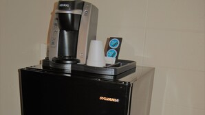 Une machine à café noire dotée d’une interface numérique et d’un porte-tasse, portant la marque « Sylvania », posée sur un sol carrelé.