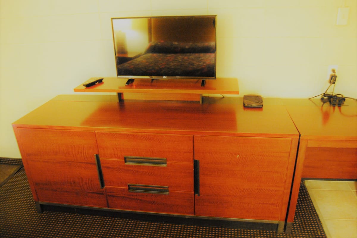 Uma cômoda de madeira com uma TV de tela plana em cima, um controle remoto e um pequeno dispositivo eletrônico no lado direito.
