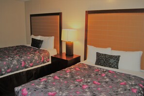 A hotel room with two beds, each with a floral-patterned bedspread, a bedside lamp, and a nightstand. - Derrick Motel (Edmonton)