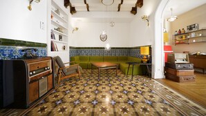 A vintage-style living room with a patterned floor, a green sofa, a wooden coffee table, and a kitchenette area with a radio and shelves. - Numa Barcelona Roca (Barcelona)