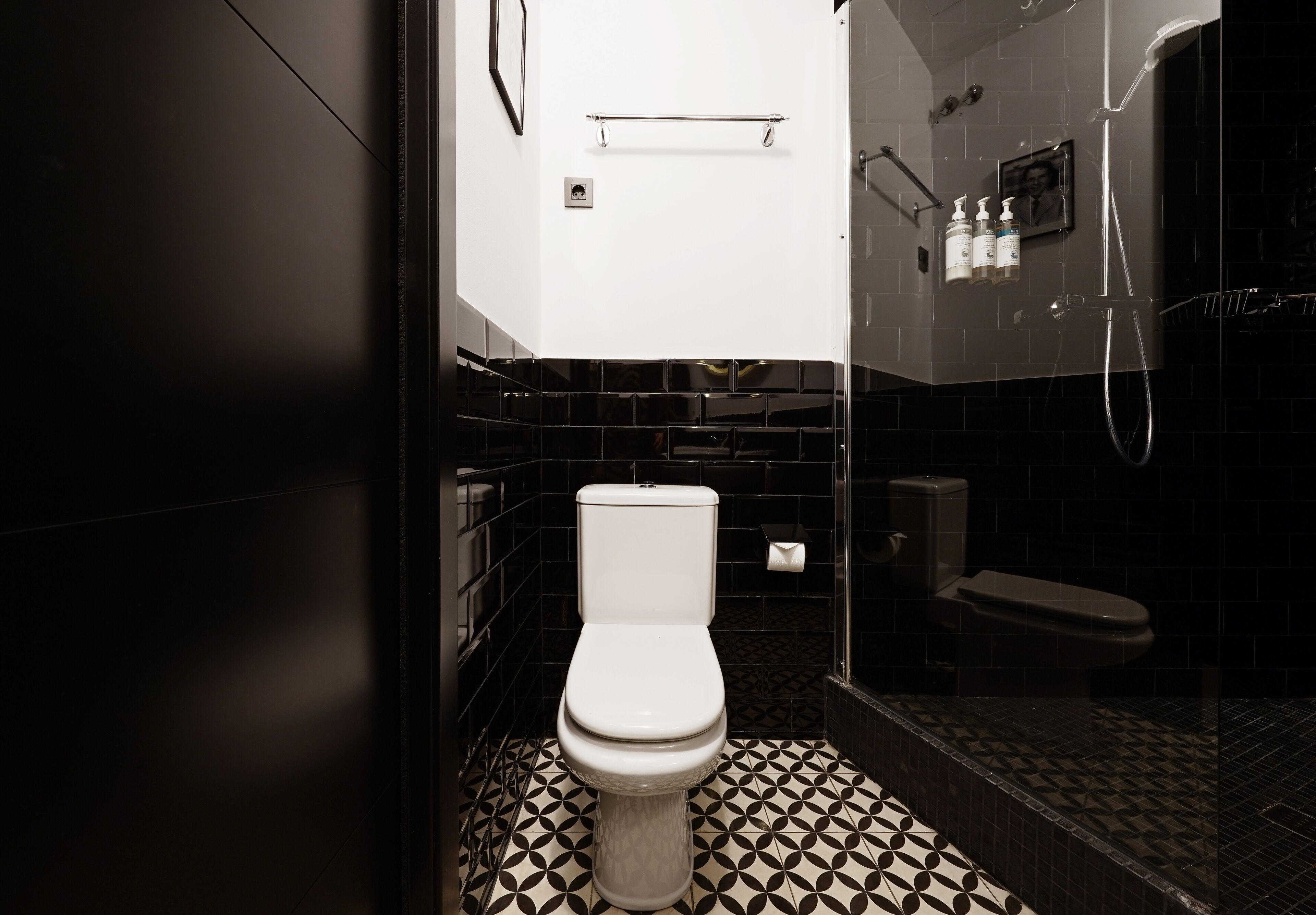 A modern bathroom with a white toilet, black and white patterned floor tiles, and a glass shower enclosure.