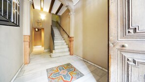 A hallway with a marble floor, a patterned rug, a staircase with a wooden handrail, and a door with a geometric design. - Numa Barcelona Roca (Barcelona)