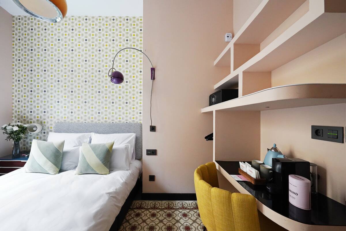 Habitación de hotel con cama, escritorio, silla, lámpara y papel tapiz estampado en la pared.
