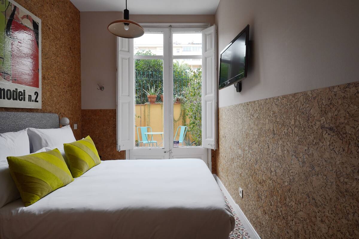 Un dormitorio con cama, almohadas, televisión, ventana y vistas al exterior.