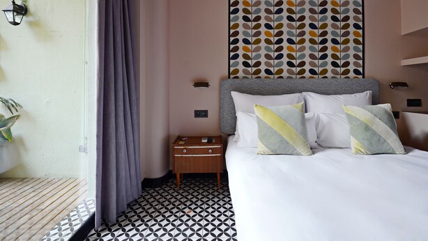 A hotel room with a bed, a nightstand, a wall with a leaf pattern, and a window with curtains. - Numa Barcelona Roca (Barcelona)