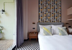 A hotel room with a bed, a nightstand, a wall with a leaf pattern, and a window with curtains. - Numa Barcelona Roca (Barcelona)