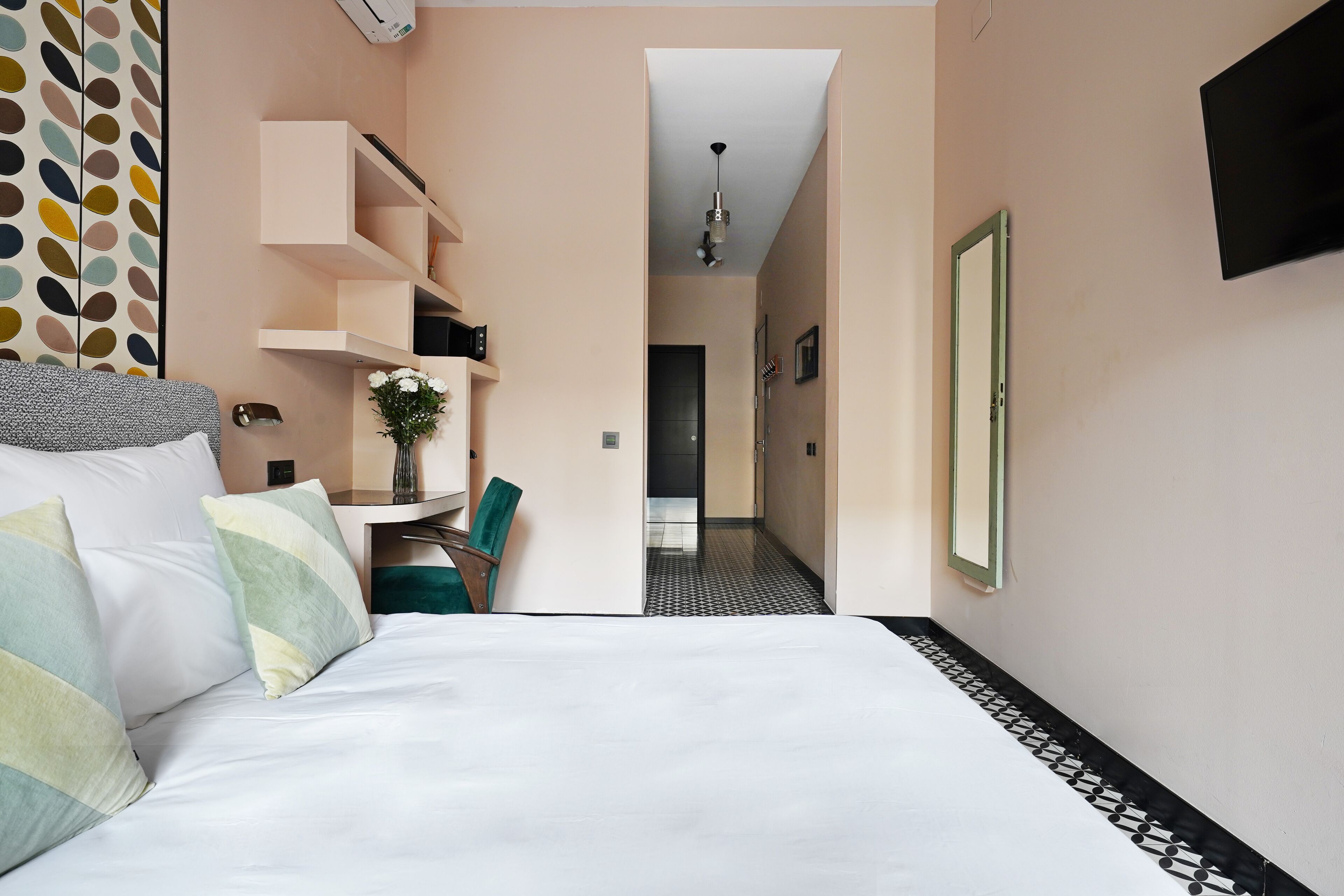 Habitación de hotel con cama, escritorio, silla, televisor y puerta que da a otra habitación.