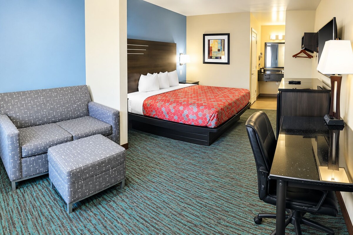 A hotel room with a sofa, a bed with a red patterned bedspread, a desk with a lamp, and a television.