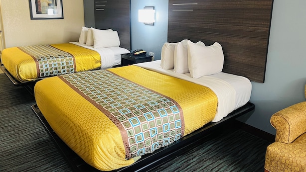 A hotel room with two beds, each with yellow and patterned bedding, a dark headboard, a bedside table with a phone, and a framed picture on the wall. - Garden Inn and Suites Little Rock (Little Rock)