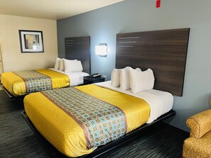 A hotel room with two beds, each with yellow and patterned bedding, a dark headboard, a bedside table with a phone, and a framed picture on the wall.