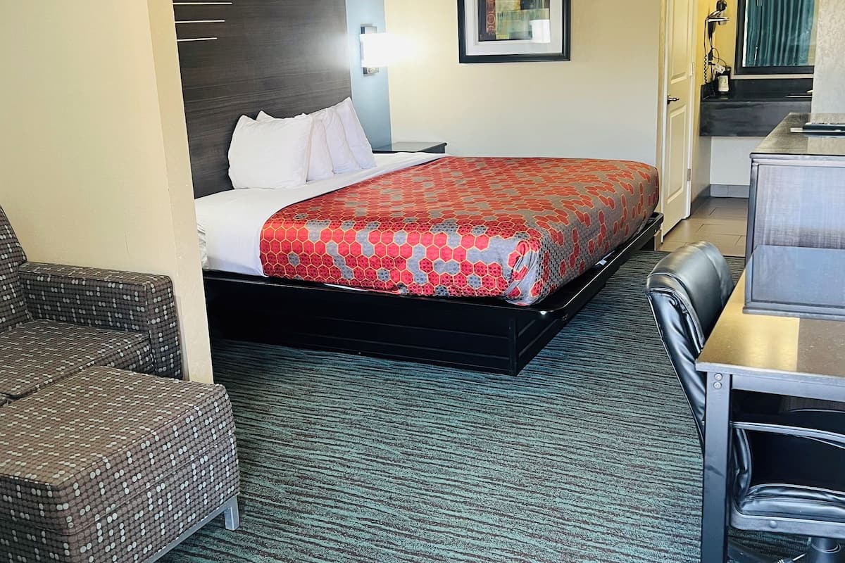 A hotel room with a bed, a chair, a desk, and a small kitchenette.
