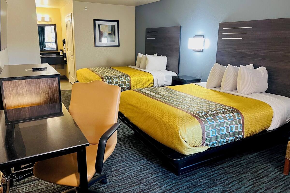 A hotel room with two beds, a desk, a chair, and a small table.