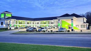 A multi-story hotel with a modern design, featuring a parking lot with several cars and a green-lit entrance. - Garden Inn and Suites Little Rock (Little Rock)