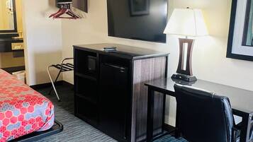 Quarto de hotel com cama, escrivaninha, cadeira, televisão, abajur e cabideiro.