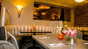Un restaurante con un rincón de estar acogedor, que incluye un banco a rayas y mesas con velas y flores.