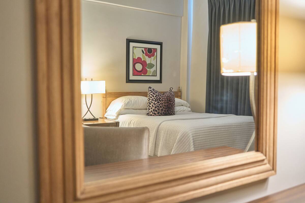 Una habitación de hotel con una cama, una mesita de noche, una lámpara y una obra de arte floral enmarcada en la pared.