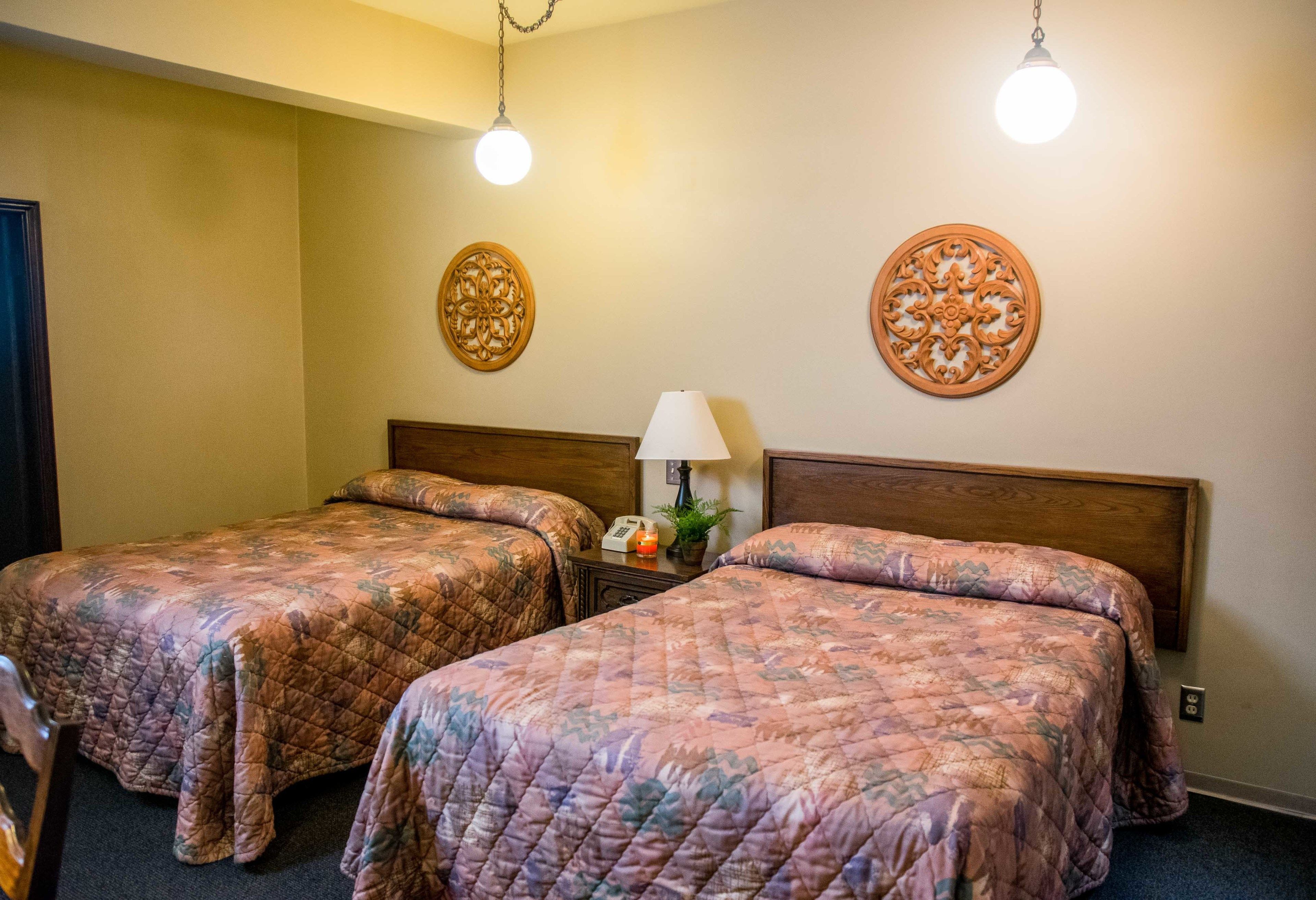 A hotel room with two beds, a nightstand, a lamp, and decorative wall art.