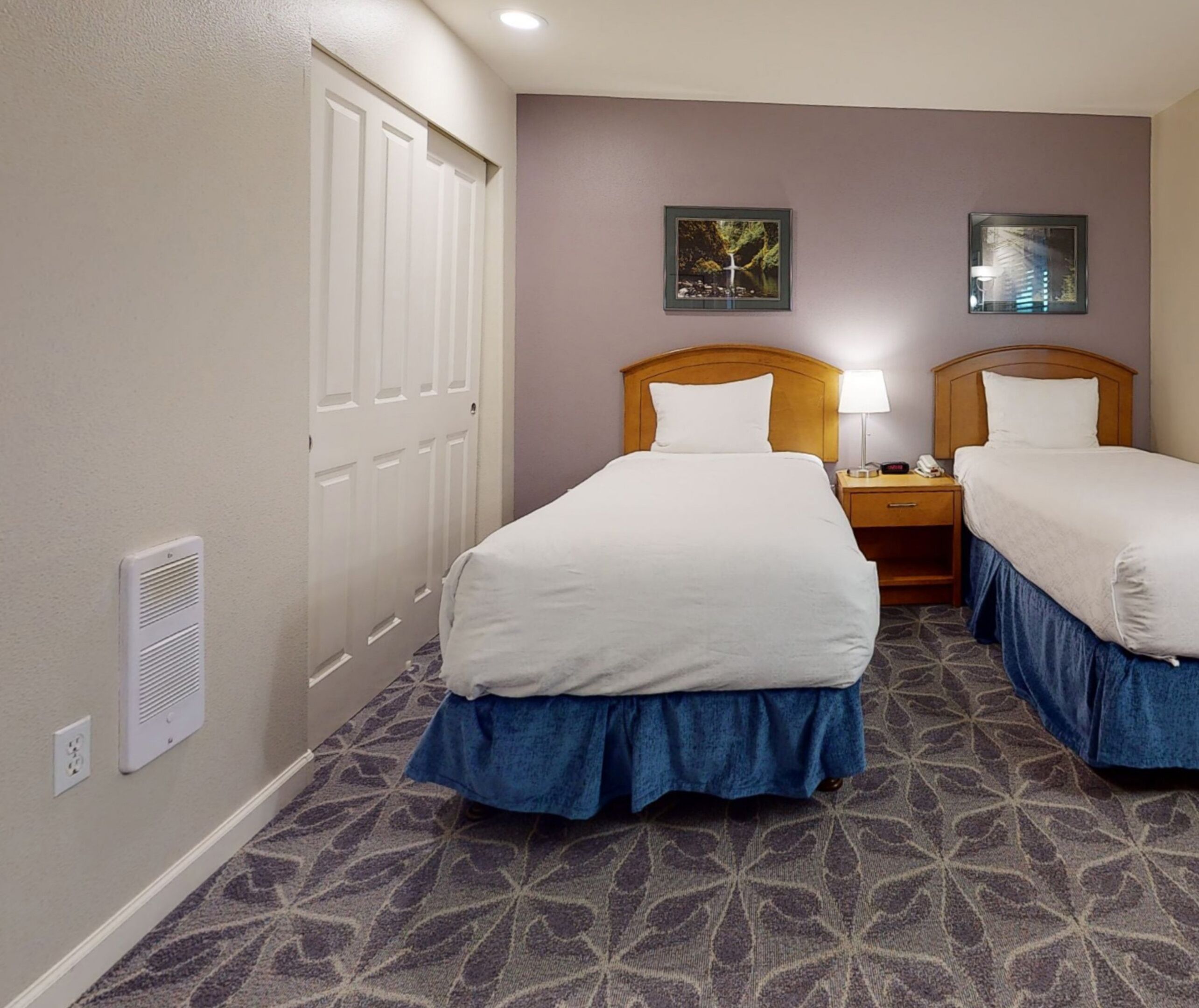 Una habitación de hotel con dos camas, una mesita de noche, una lámpara y una puerta.