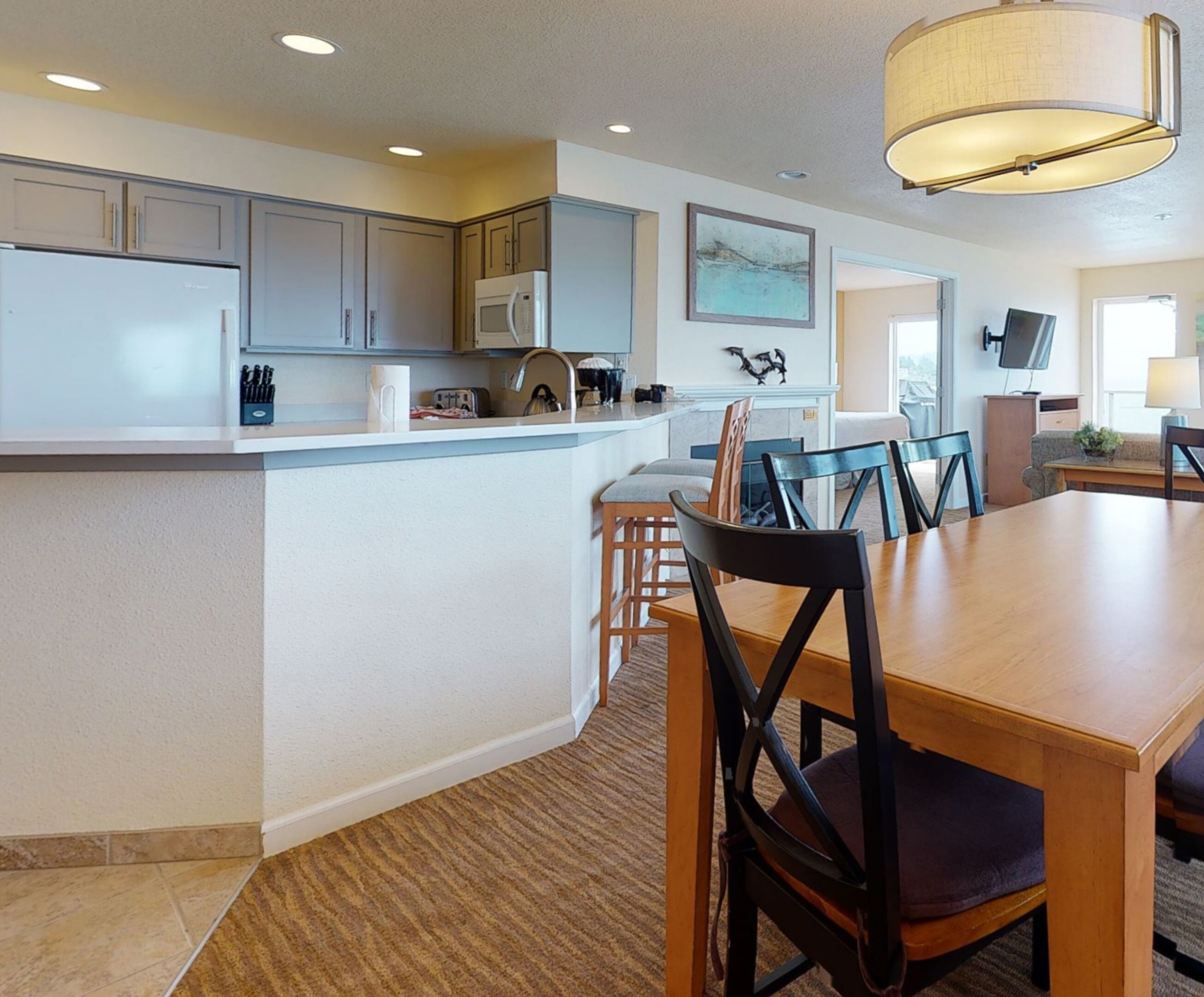 A modern kitchen with a central island, a dining area with a wooden table and chairs, and a large window providing natural light.