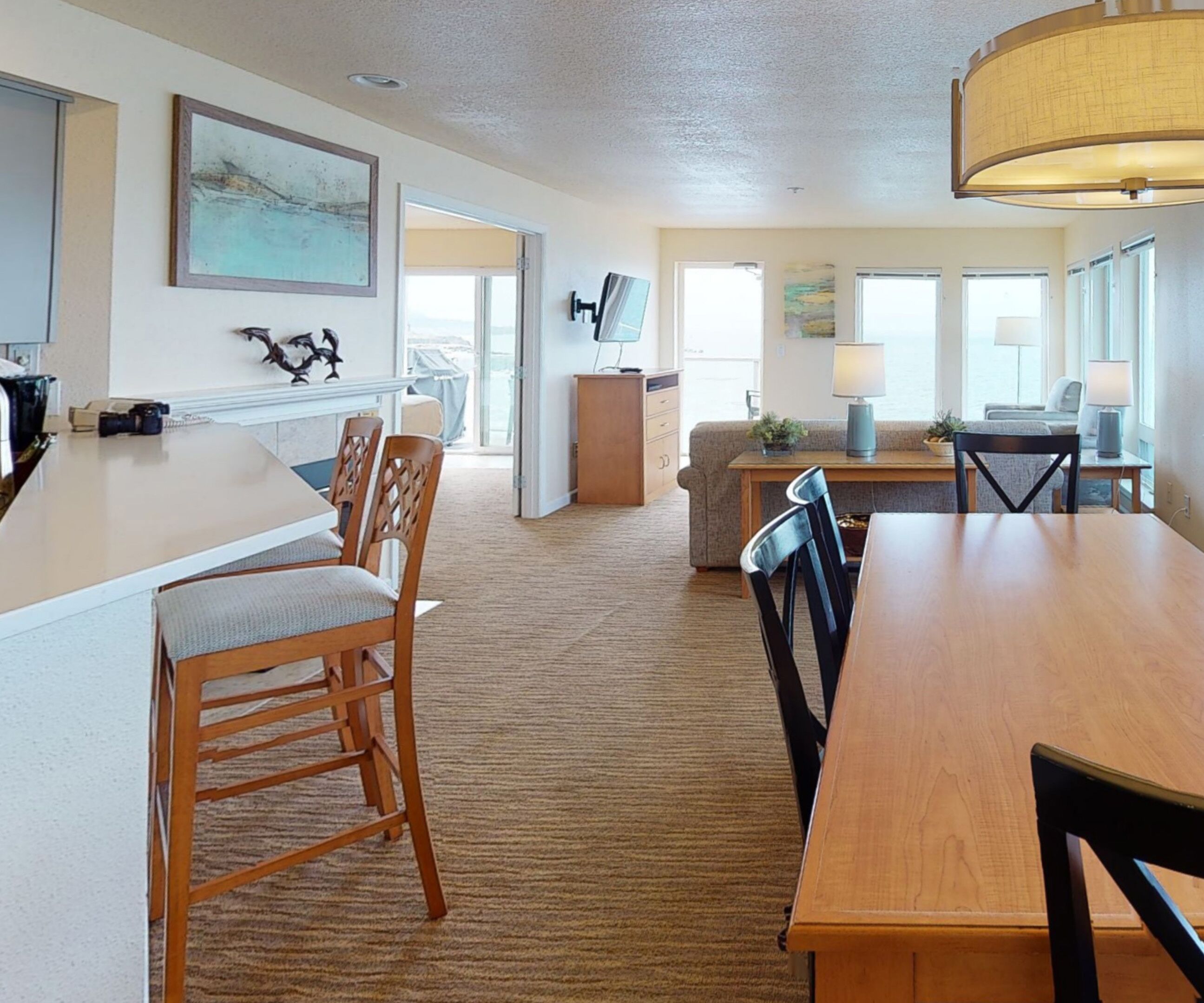 A spacious living area with a large wooden dining table, several chairs, a sofa, and a kitchen area with a countertop and cabinets.