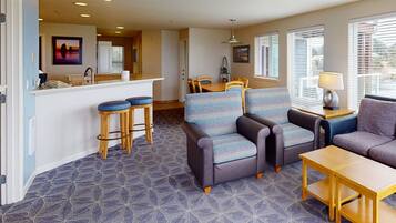 A hotel room with a kitchenette, a seating area with a sofa and chairs, a small table, and a patterned carpet.