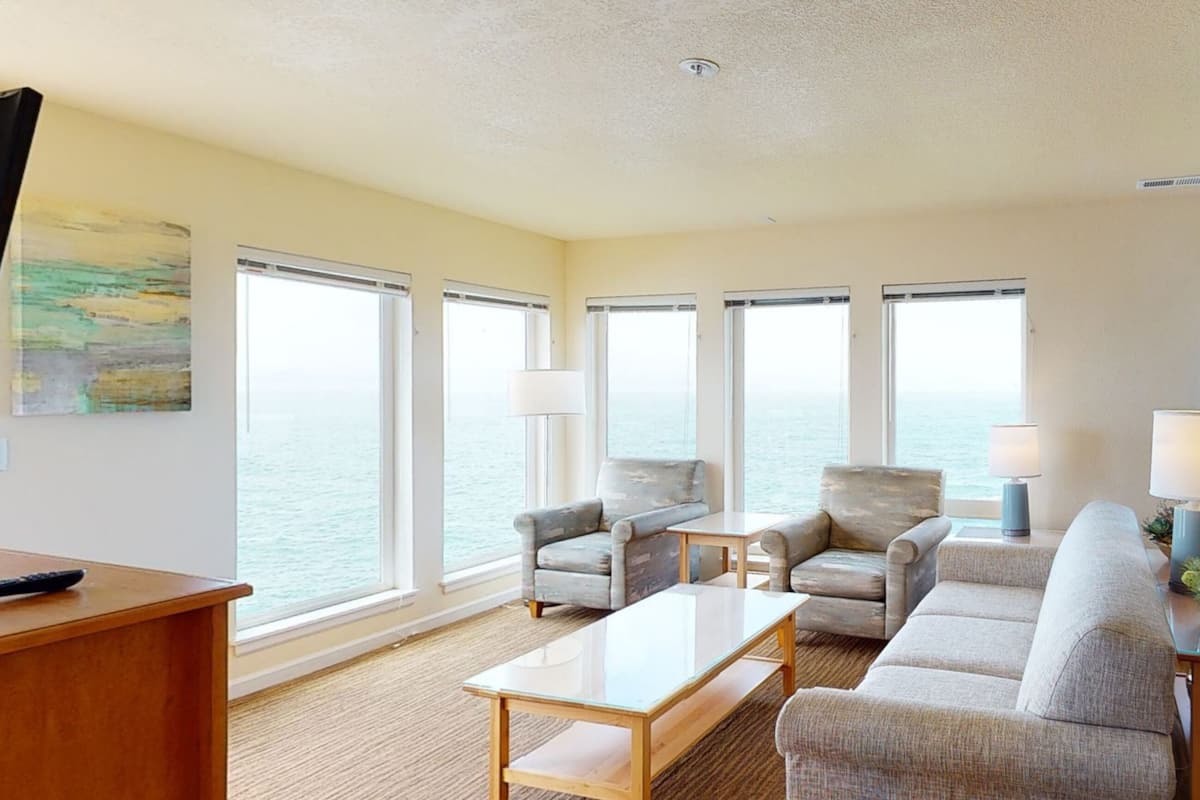 A spacious living room with large windows, a wooden coffee table, and two sofas.