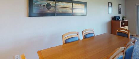 A dining area with a wooden table and blue chairs, a glass ceiling light, and a wall-mounted painting.