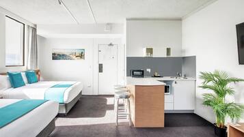 Una camera d'albergo moderna con un letto grande, un angolo cottura e una zona salotto con sgabelli.
