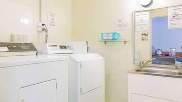 A hotel laundry room with a washing machine, dryer, and a sink. There are signs indicating laundry services and prices.