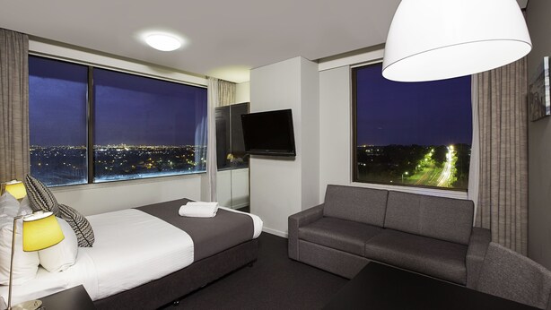 A hotel room with a bed, a sofa, a TV, and large windows offering city views. - Metro Hotel Miranda (Miranda)