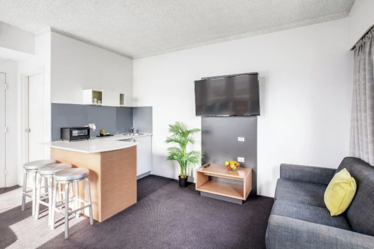 Un espacio habitable compacto con kitchenette, televisor de pantalla plana, sofá y una pequeña zona de bar.