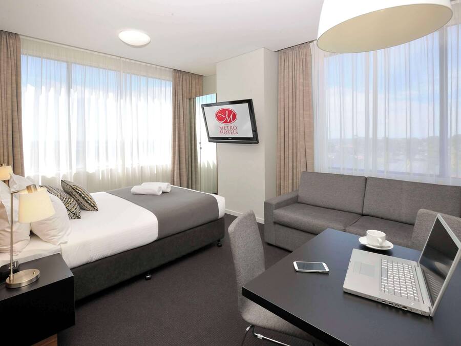 Ein Hotelzimmer mit Bett, einer Couch, einem Schreibtisch mit Laptop, einer Lampe und einem gerahmten Schild an der Wand.