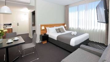 Quarto de hotel moderno com uma cama, uma mesa, uma cadeira, uma TV e uma janela com cortinas.