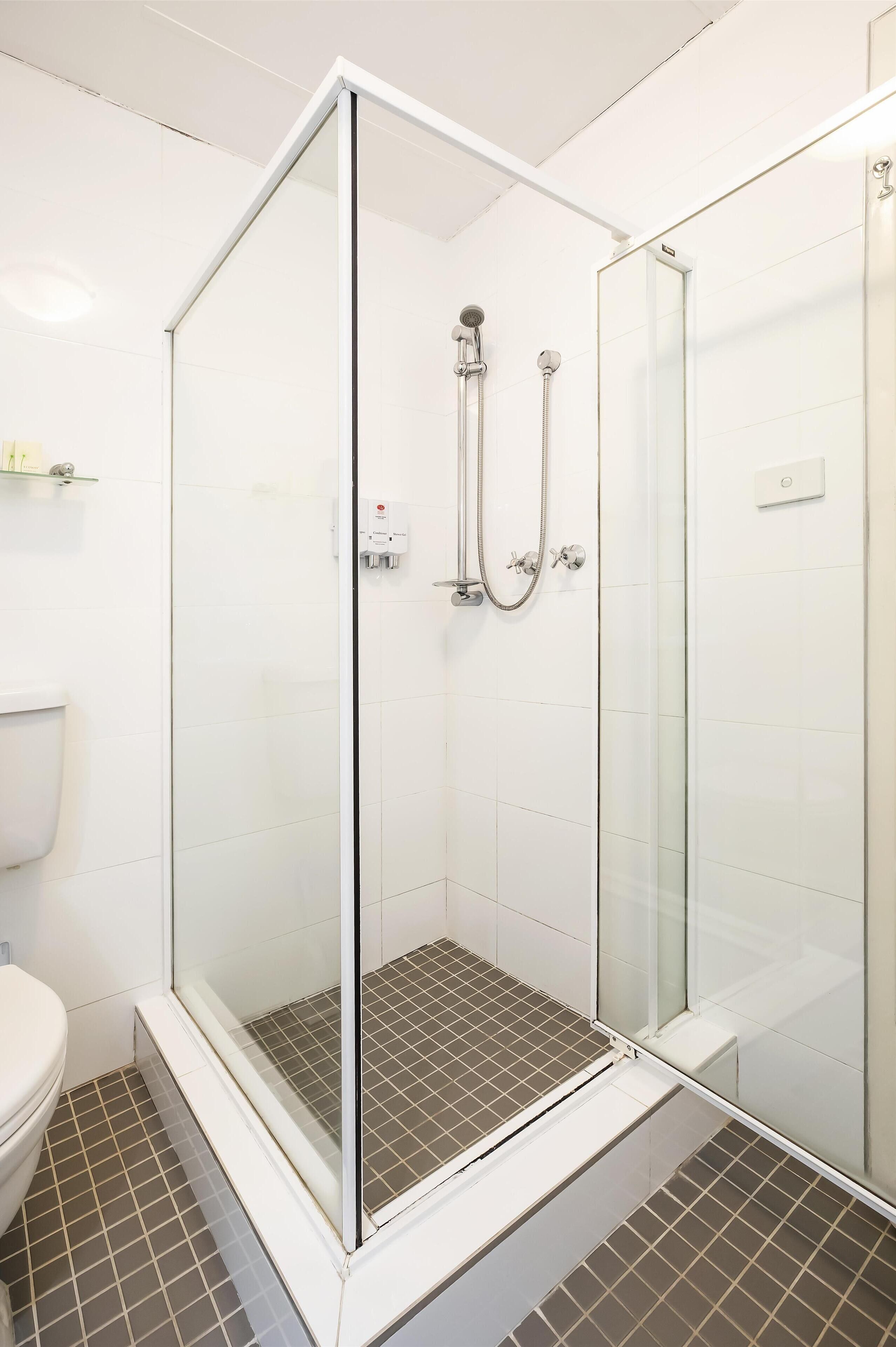 A glass-enclosed shower with a white tiled floor and a white toilet visible to the left.