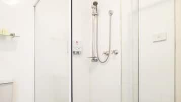 A glass-enclosed shower with a white tiled floor and a white toilet visible to the left.