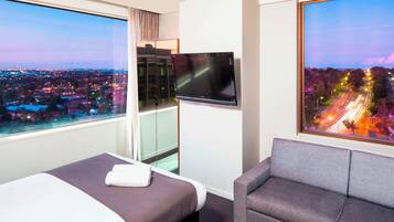 Enjoy a city view from the comfort of this stylish room, featuring a single bed, sofa, flat-screen TV, and cityscape photography.