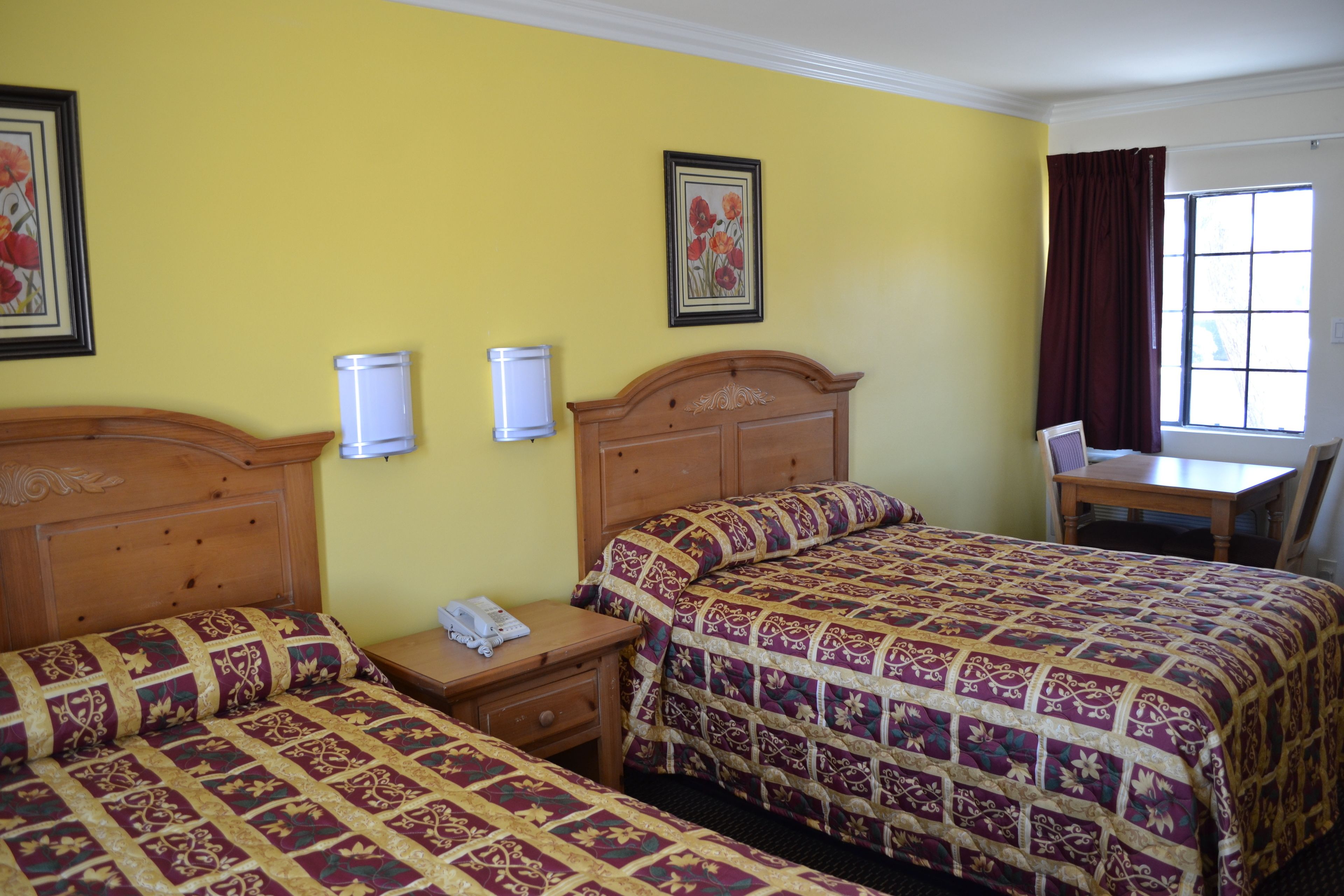Une chambre d’hôtel avec deux lits, un bureau et une chaise. Il y a deux lampes fixées au mur et une fenêtre avec des rideaux.