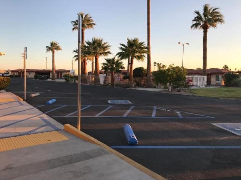 A parking lot with marked spaces, palm trees, and a building in the background.