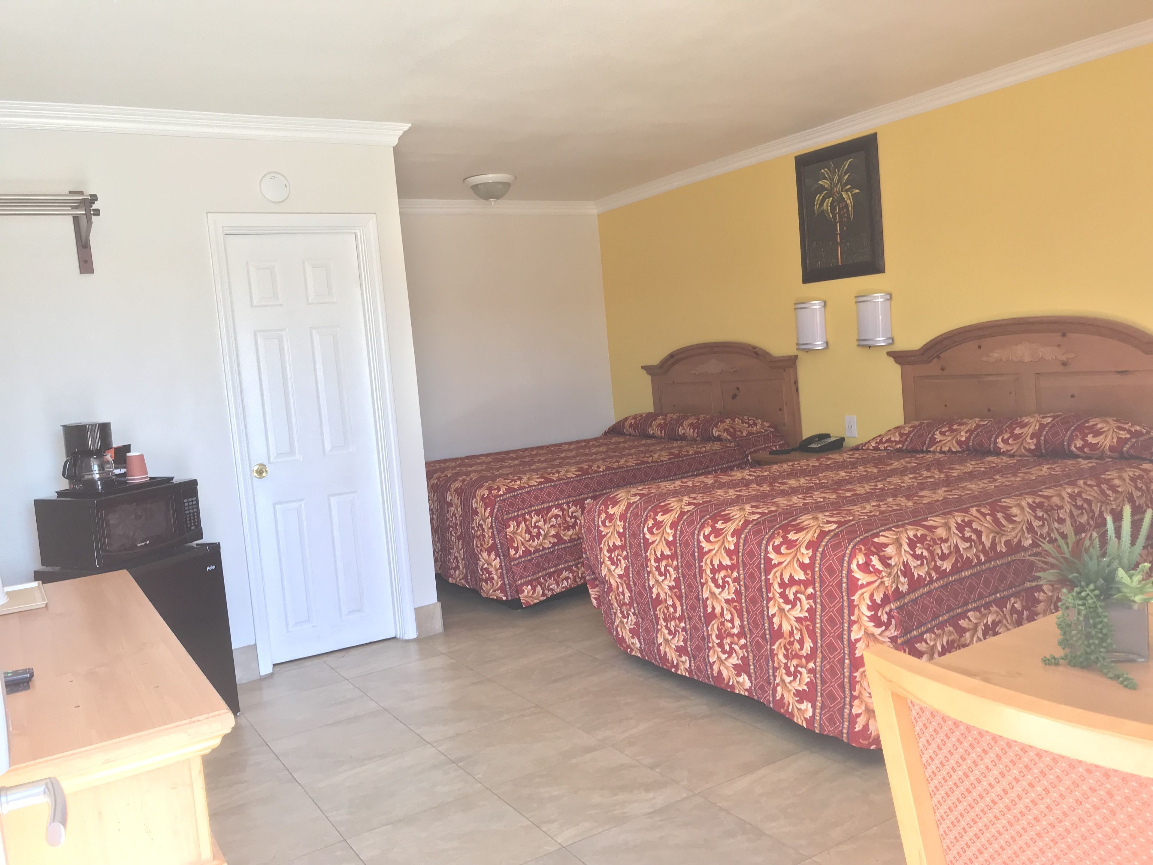 Ein Hotelzimmer mit zwei Betten, einem Holztisch, einer Mikrowelle und einer Tür.