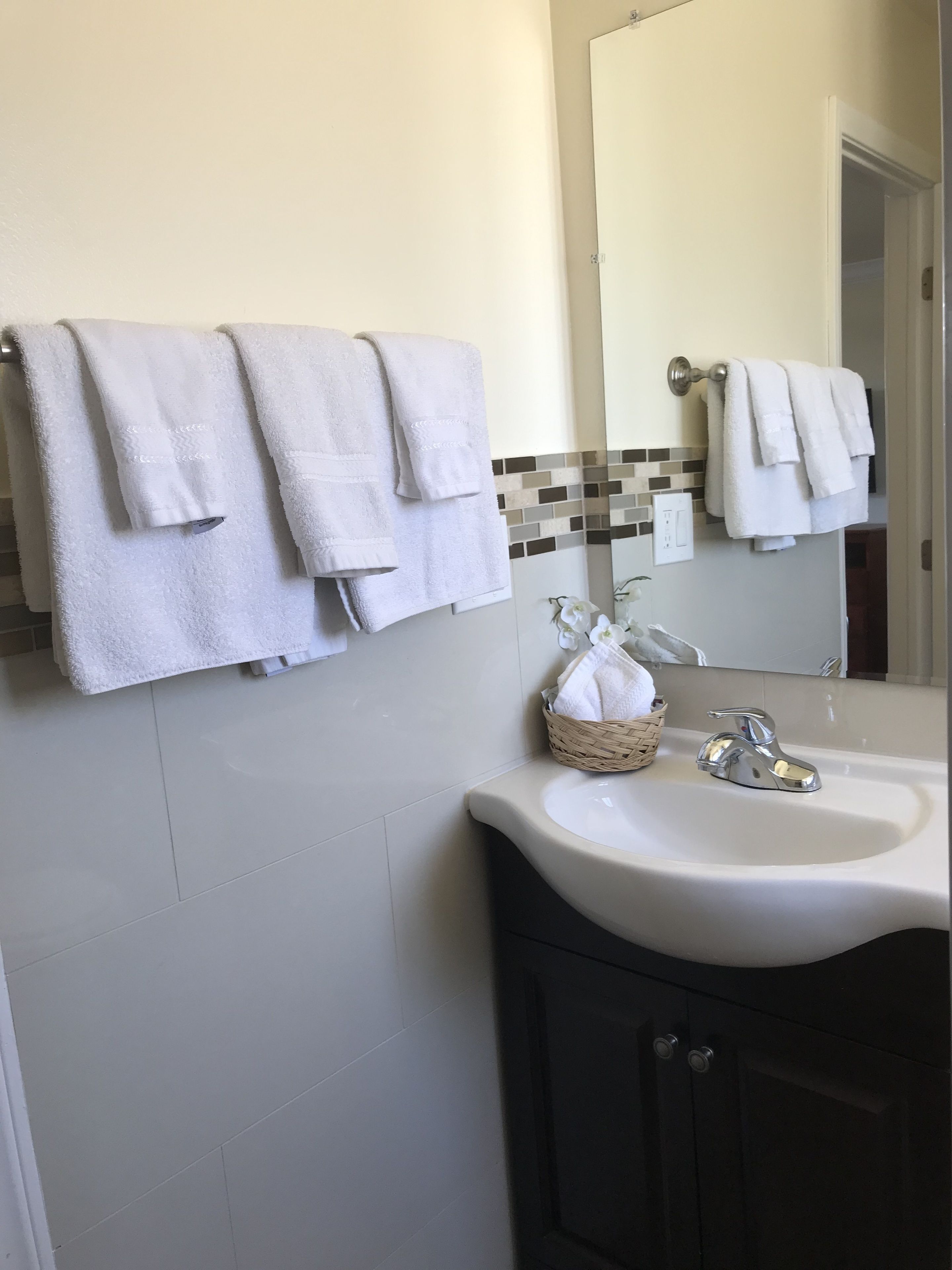 A bathroom with white towels hanging on a rack, a sink with a chrome faucet, and a mirror above the sink.