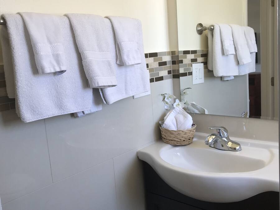 A bathroom with white towels hanging on a rack, a sink with a chrome faucet, and a mirror above the sink.