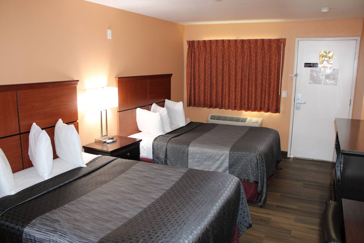 Quarto de hotel com duas camas, uma mesinha de cabeceira, uma escrivaninha e uma porta com um aviso.