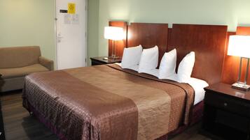 A hotel room with a large bed, a nightstand with a lamp, a chair, and a door with a sign.