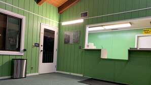 A room with green walls, a white door, a trash can, a black mat, and a sign on the wall. - Rancho California Inn (Temecula)