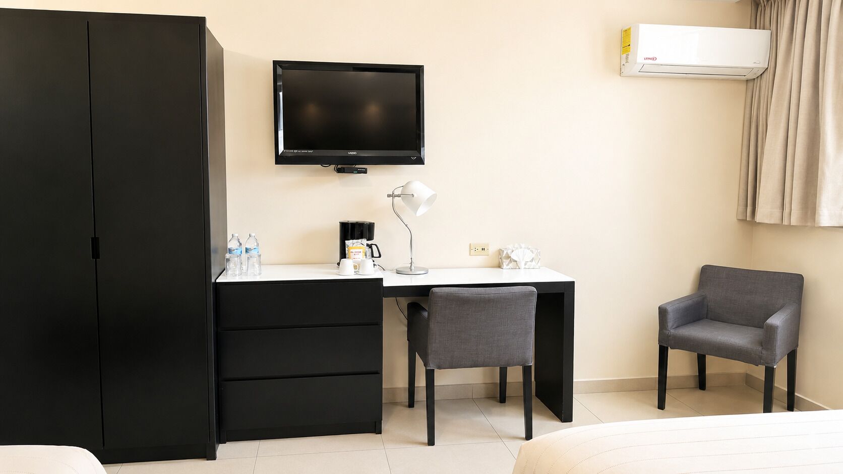 Ein Hotelzimmer mit einem Bett, einem Schreibtisch mit Stuhl, einem Fernseher, einer Klimaanlage und einem Kleiderschrank.